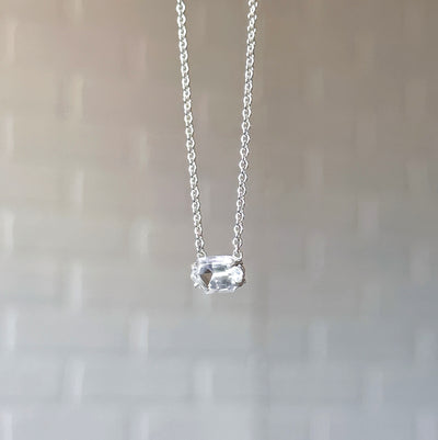 Emerson Quartz Necklace in Silver hanging in front of a white brick wall, side angle