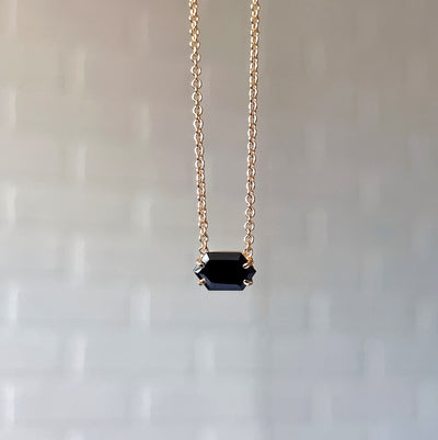 Emerson Black Garnet Necklace in Vermeil hanging in front of a white brick wall, front angle