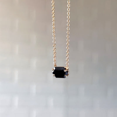 Emerson Black Garnet Necklace in Vermeil hanging in front of a white brick wall, side angle