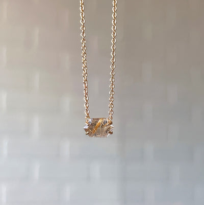 Emerson Rutilated Quartz Necklace in Vermeil hanging in front of a white brick wall, front angle