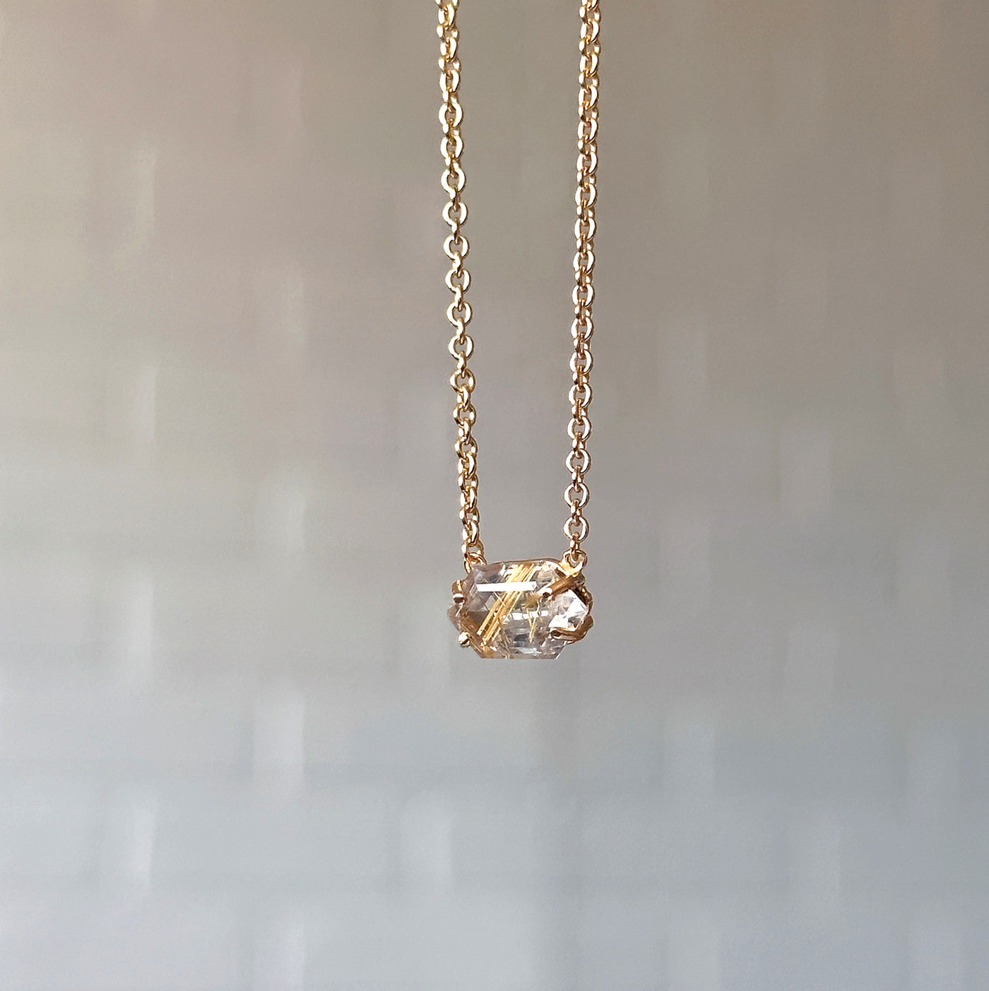 Emerson Rutilated Quartz Necklace in Vermeil hanging in front of a white brick wall, side angle