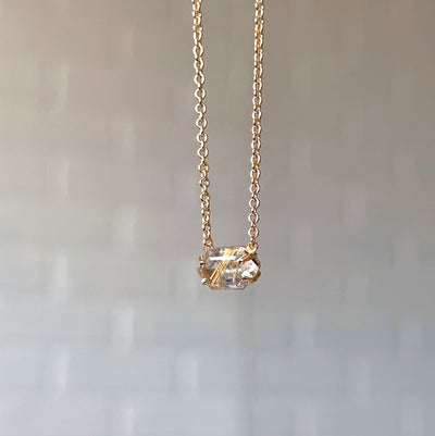 Emerson Rutilated Quartz Necklace in Vermeil hanging in front of a white brick wall, side angle