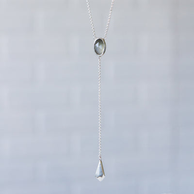 Grey Moonstone Lariat #1 hanging in front of a gray wall
