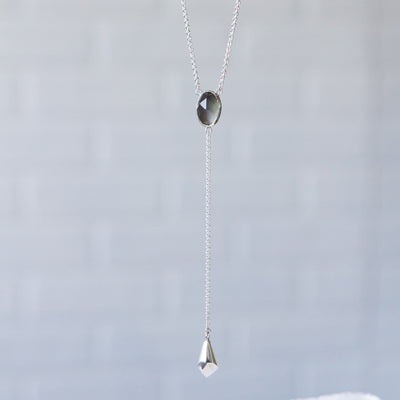 Grey Moonstone Lariat #2 hanging in front of a gray wall