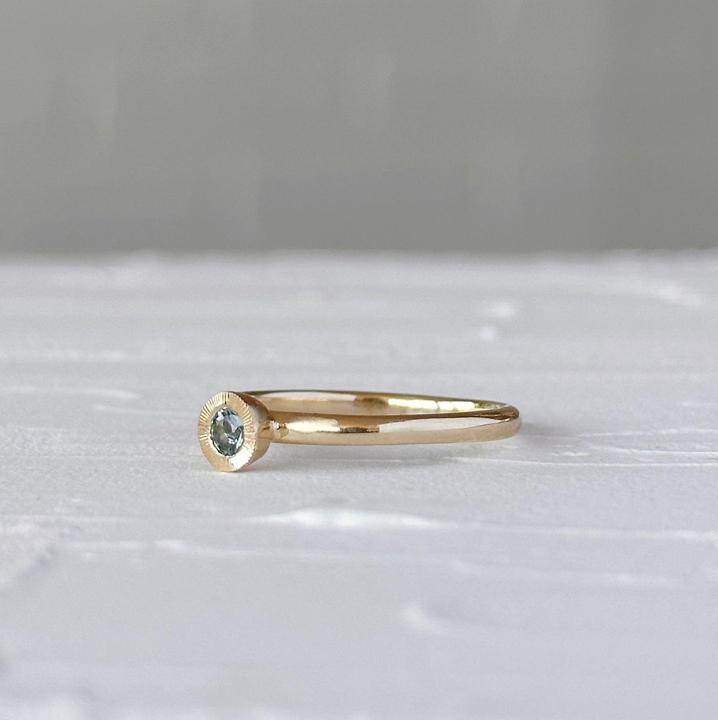 Teal Montana Sapphire Large Aurora Stacking Ring in Yellow Gold on a white table, side angle