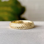 Herringbone Wide Band in gold on a gray background
