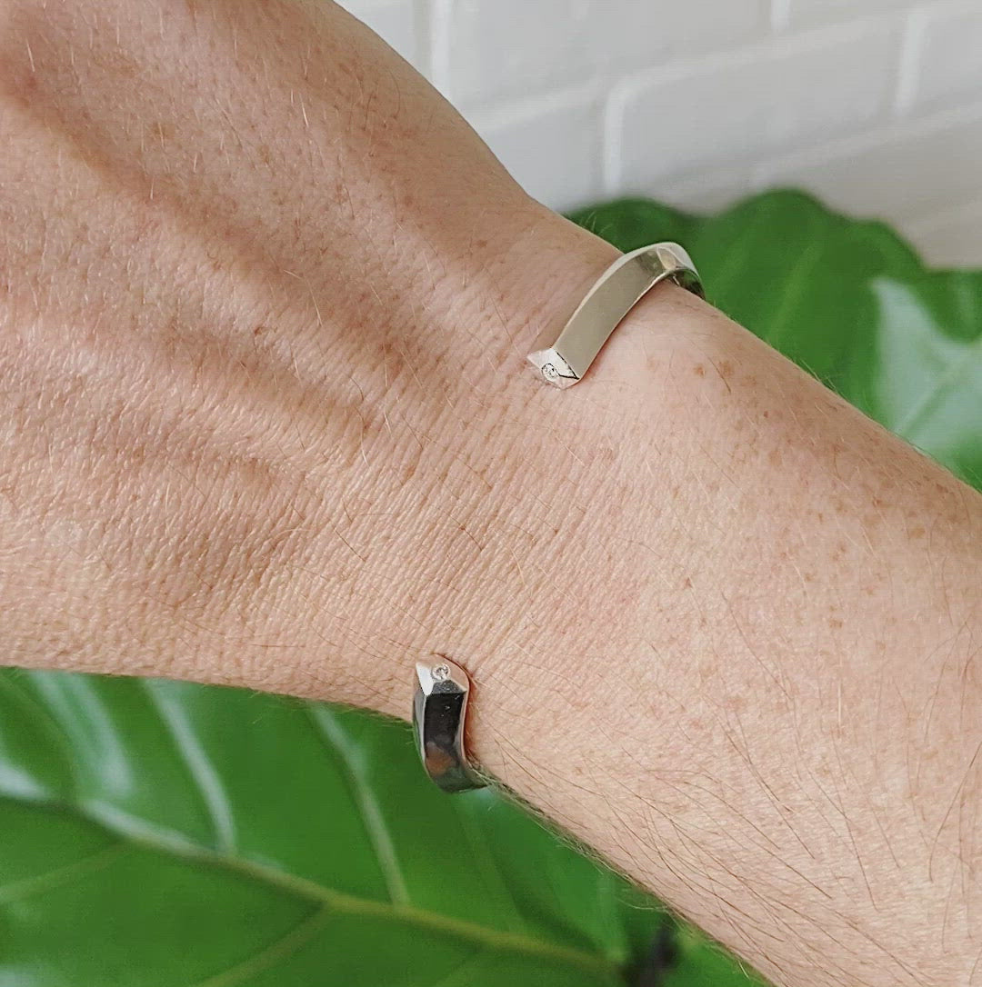Faceted sterling silver cuff with pentagon faceted ends and a single diamond in each on a wrist by Corey Egan