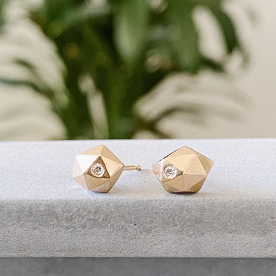 Geometric faceted gold wabi-sabi stud earrings with white diamonds in 14k yellow gold by Corey Egan on concrete side view