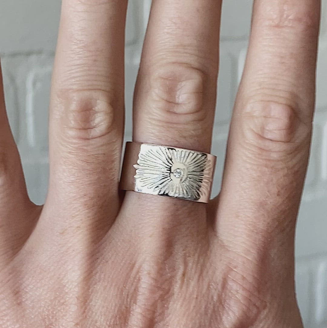Sterlign silver wide band with single diamond and a carved sunburst design on a hand by Corey Egan