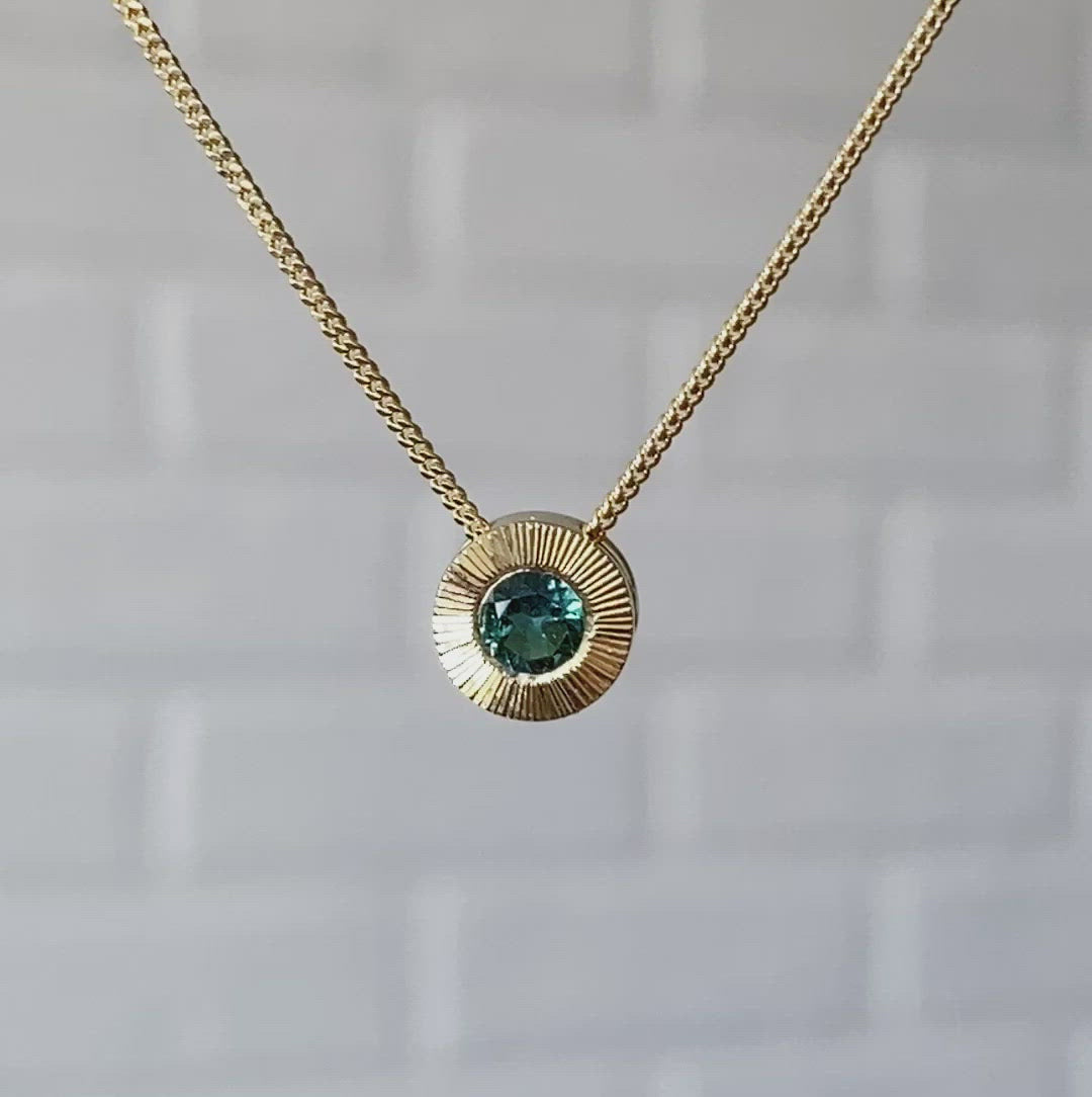 14k yellow gold medium Aurora necklace with a round teal green indicolite tourmaline center and engraved rays halo border