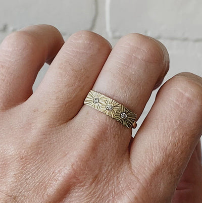 Yellow gold bar ring with three diamonds and a carved sunburst design around each by Corey Egan on a hand