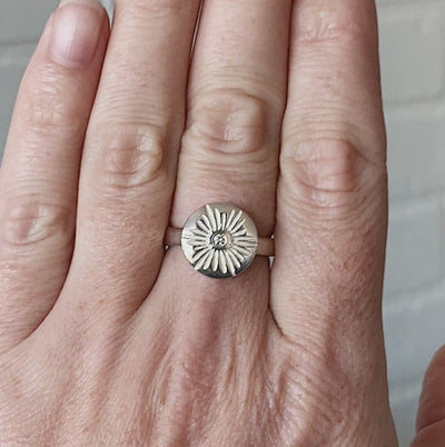 Large carved sunburst ring with a diamond center in sterling silver on a hand by Corey Egan