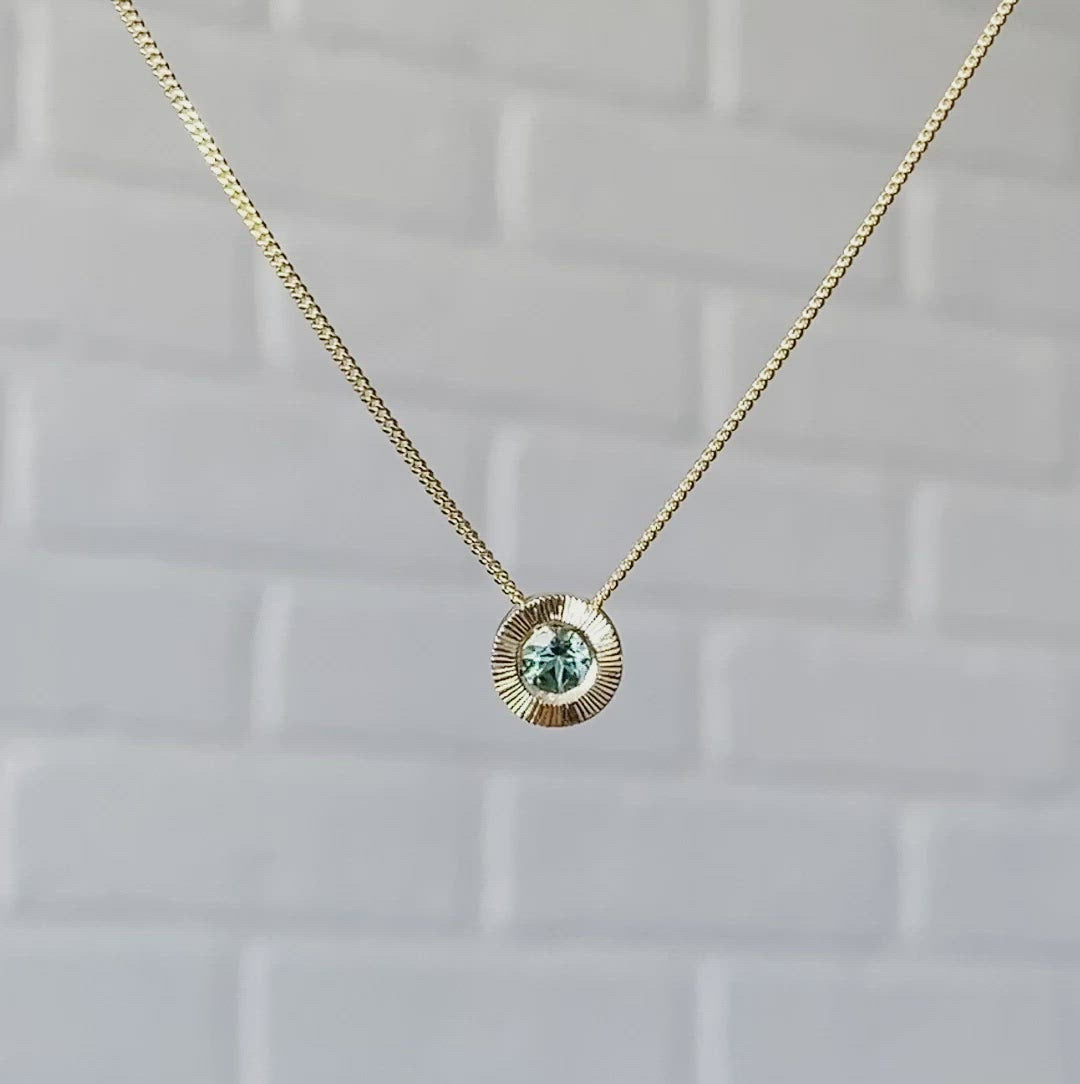 14k yellow gold medium Aurora necklace with a round seafoam green tourmaline center and engraved rays halo border