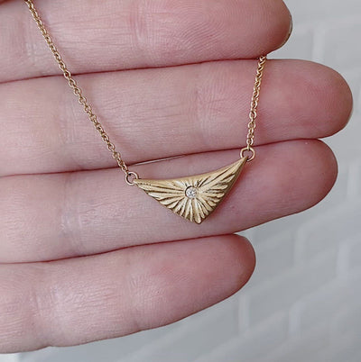 Triangular gold flash necklaw eith a diamond center and sunburst carved motif in 14k yellow gold in a hand by Corey Egan