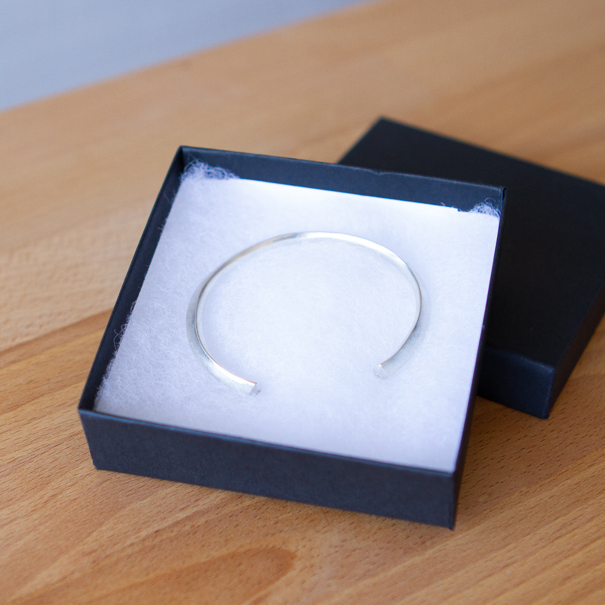 Faceted sterling silver cuff with pentagon faceted ends and a single diamond in each in a gift box by Corey Egan