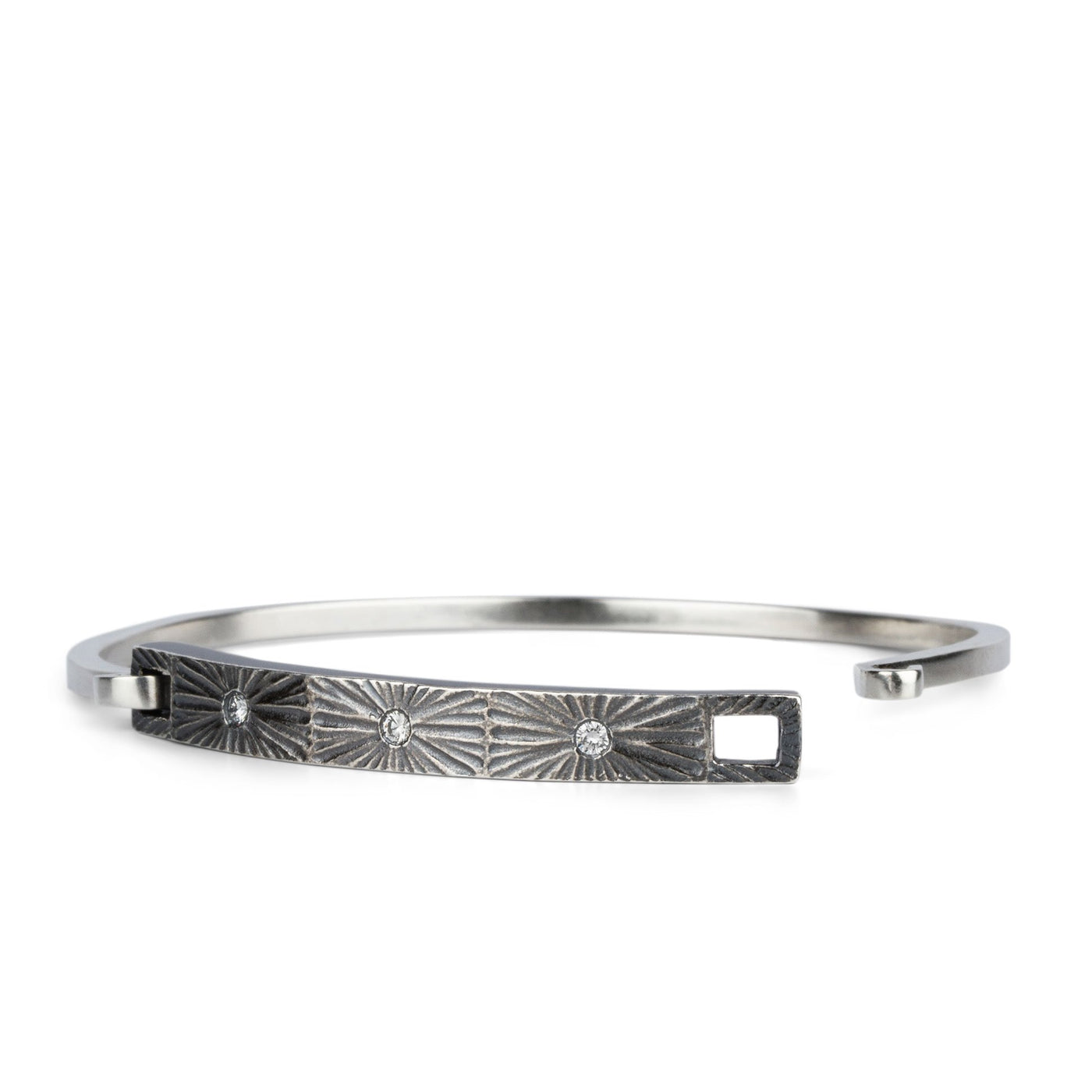 Oxidized sterling silver bar bracelet with three diamonds and a carved sunburst around each by Corey Egan on a white background side view #1