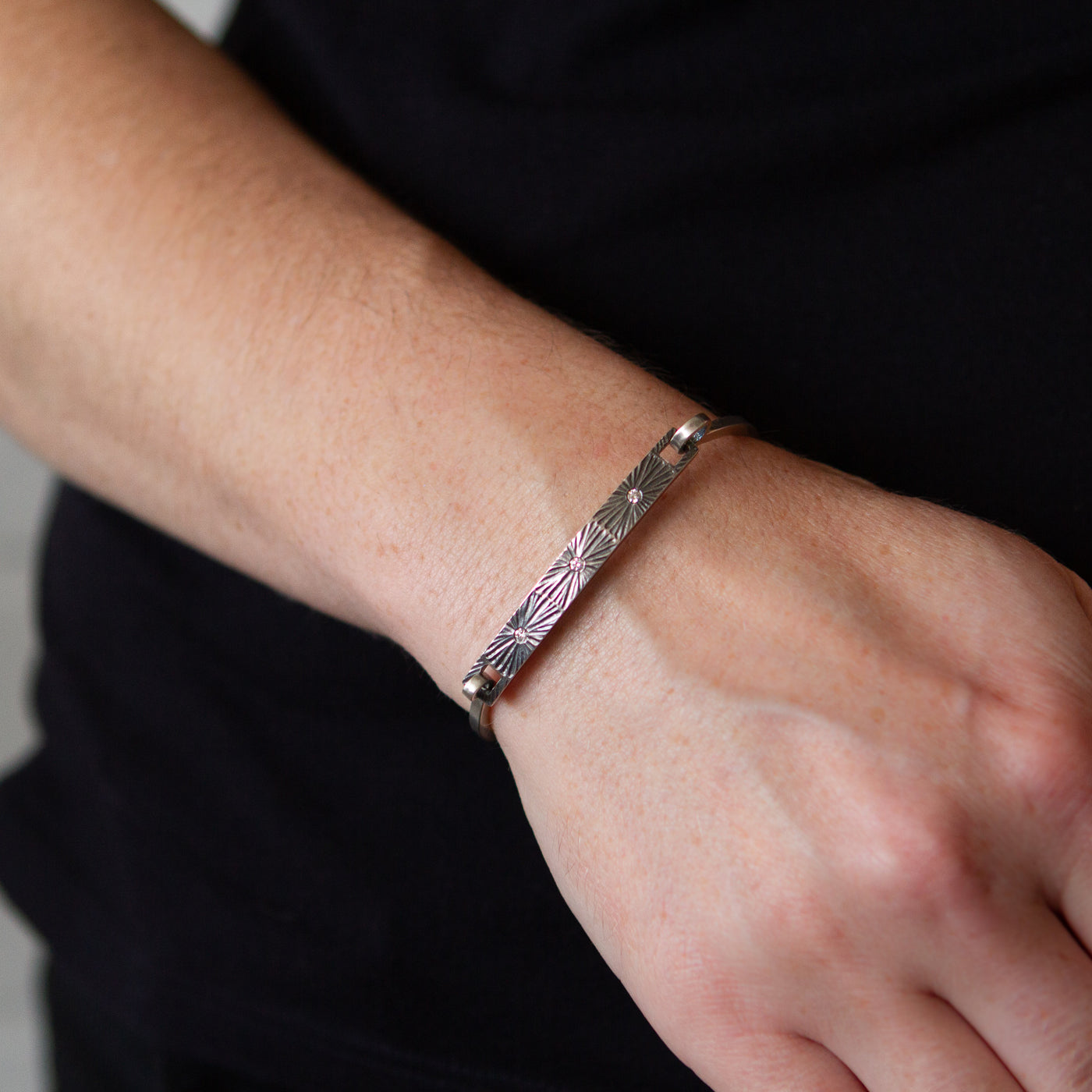 Oxidized sterling silver bar bracelet with three diamonds and a carved sunburst around each on a wrist by Corey Egan
