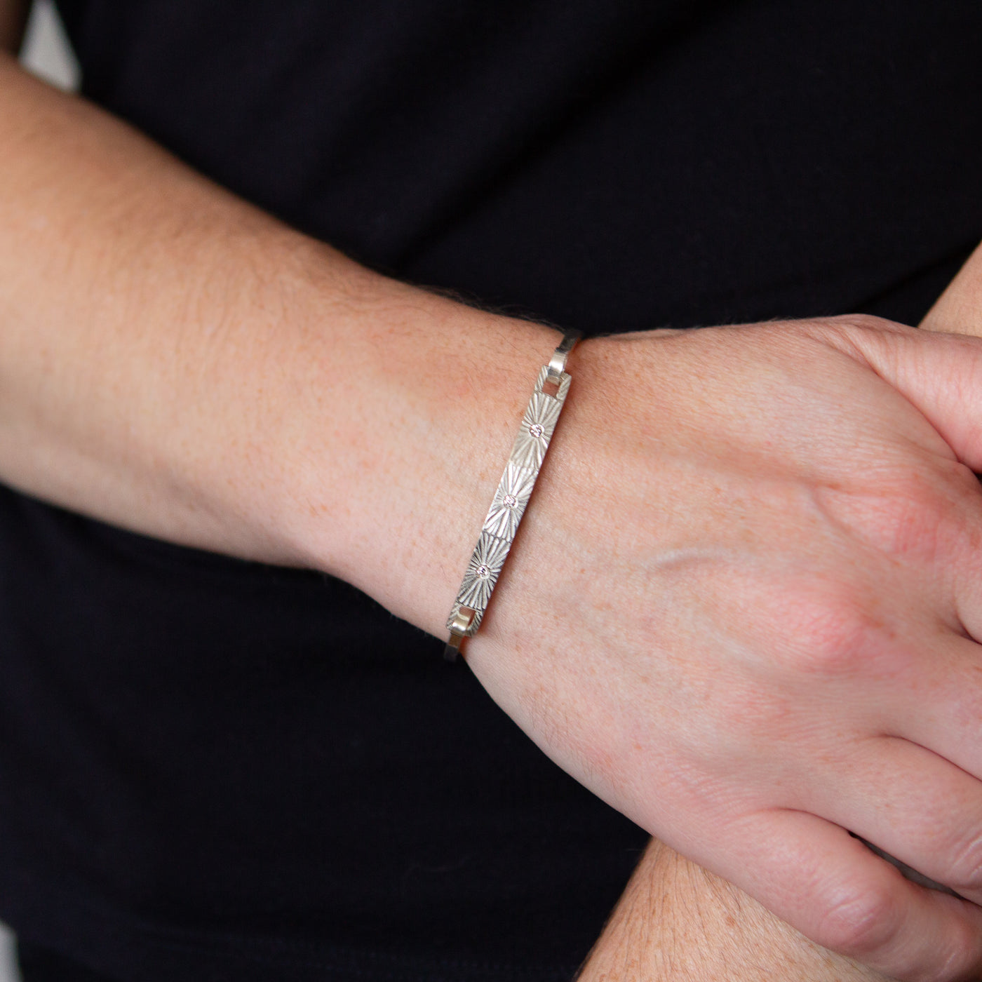 Sterling silver bar bracelet with three diamonds and a carved sunburst around each on a wrist by Corey Egan