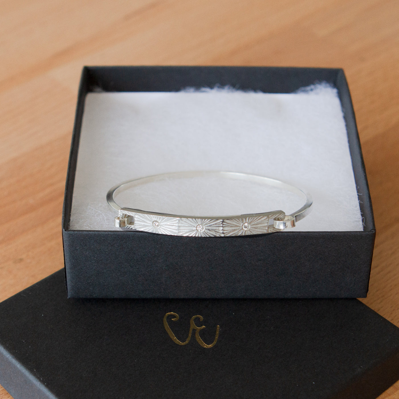 Sterling silver bar bracelet with three diamonds and a carved sunburst around each by Corey Egan in a gift box
