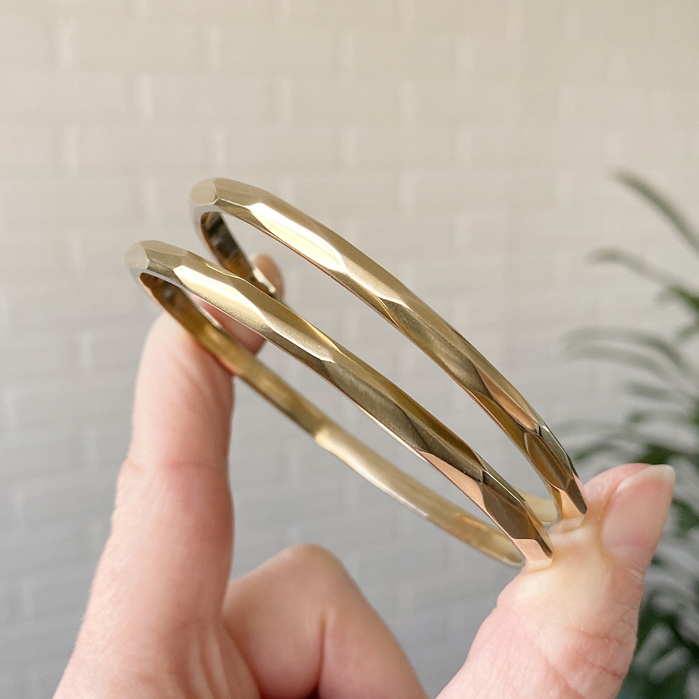 stackable faceted yellow bronze bangle bracelets held between two fingers