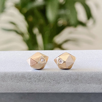 Geometric faceted gold wabi-sabi stud earrings with white diamonds in 14k yellow gold by Corey Egan on concrete
