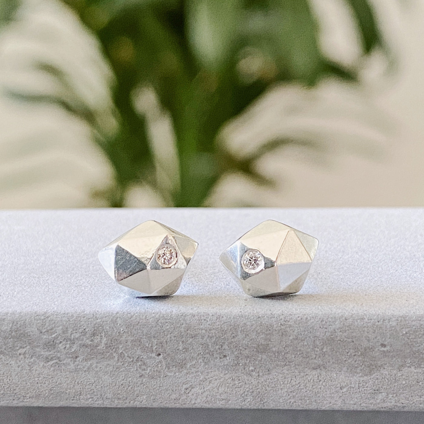 Sterling silver wabi-sabi faceted geometric stud earrings with two flush set diamonds by Corey Egan on concrete front view