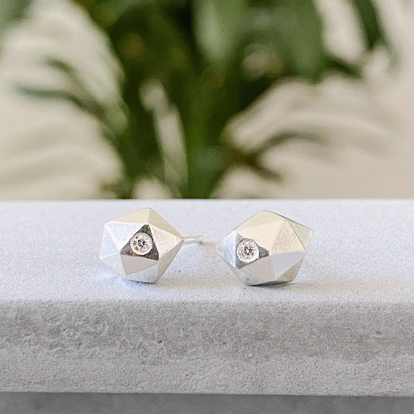 Sterling silver wabi-sabi faceted geometric stud earrings with two flush set diamonds by Corey Egan on concrete