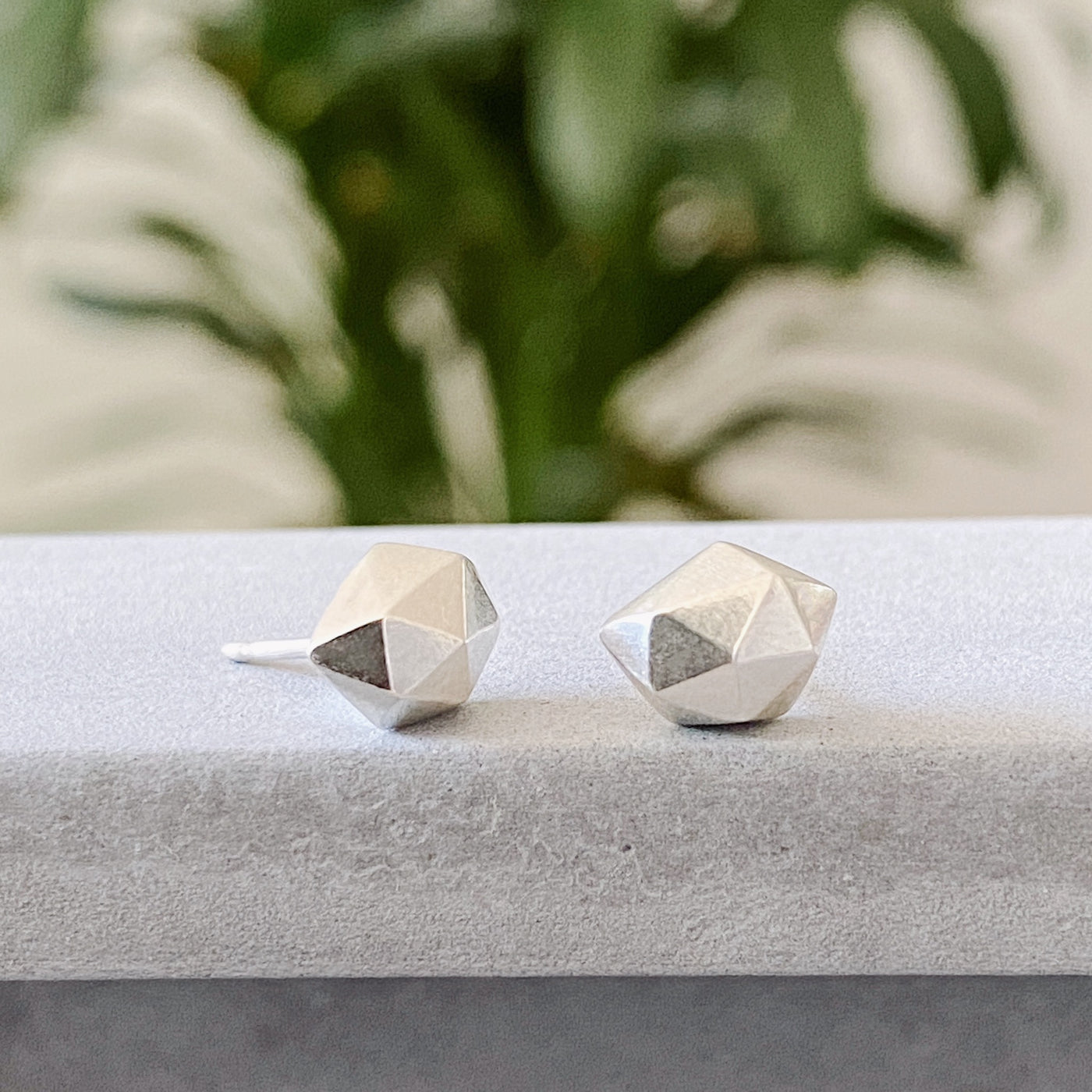 Sterling silver wabi-sabi faceted geometric stud earrings by Corey Egan on concrete side view