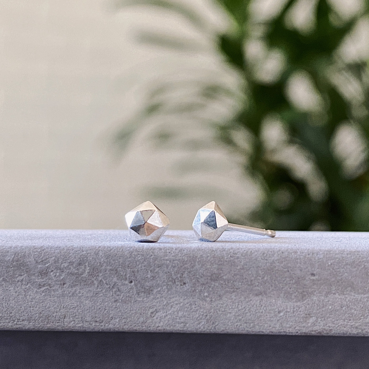 sterling silver micro size geometric faceted stud earrings by Corey Egan side view on concrete
