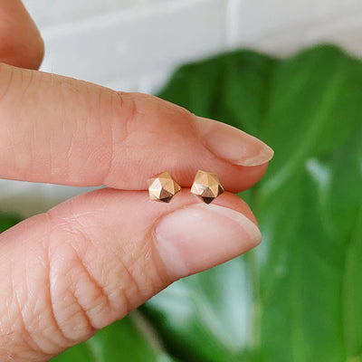 extra small faceted rose gold micro fragment stud earrings between a pair of fingers