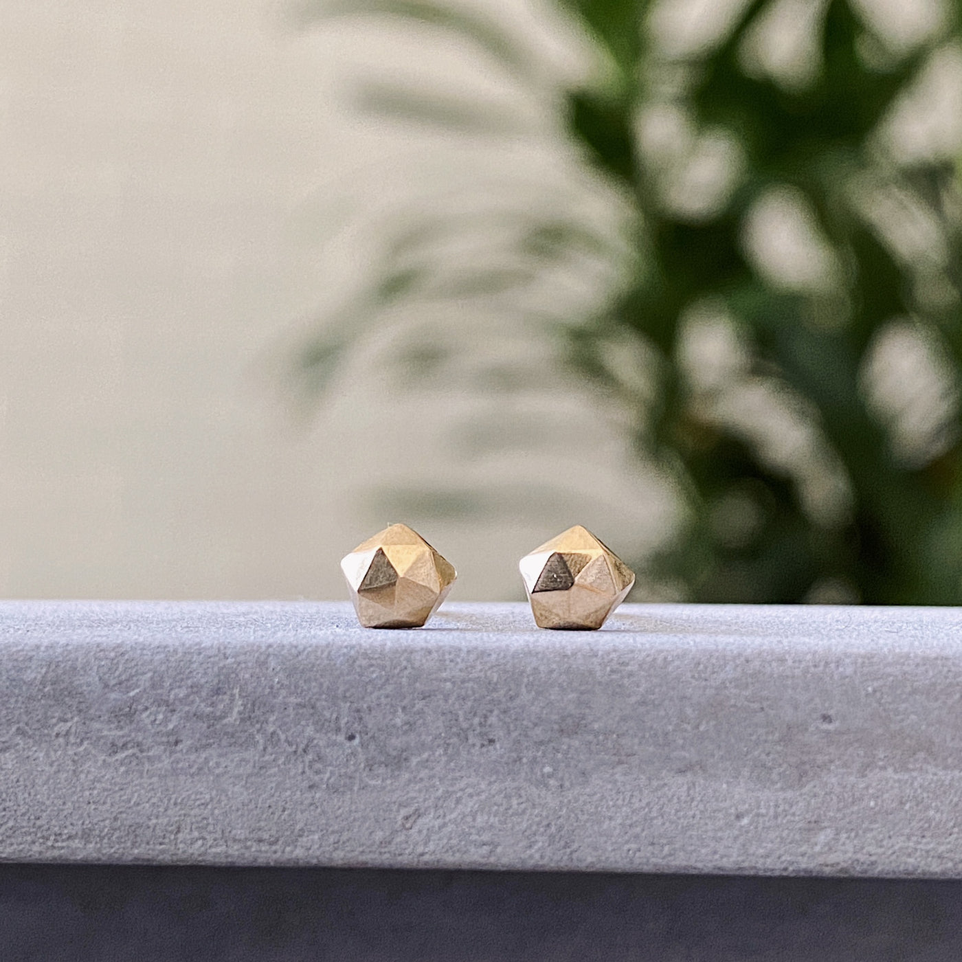 14k yellow gold geometric faceted stud earrings in the micro size on concrete by Corey Egan