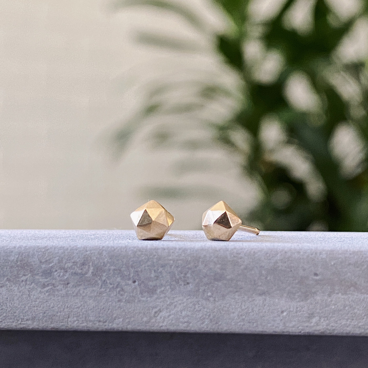 14k yellow gold geometric faceted stud earrings in the micro size on concrete side view by Corey Egan