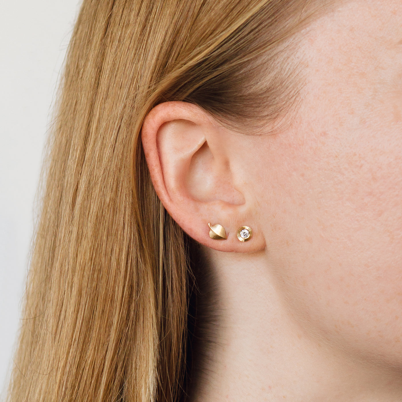 gold aspen leaf stud earrings with diamond aurora stud earrings on an ear