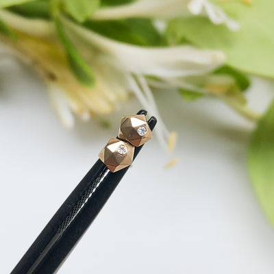 14k yellow gold geometric faceted stud earrings with diamonds in the micro size held by tweezers by Corey Egan