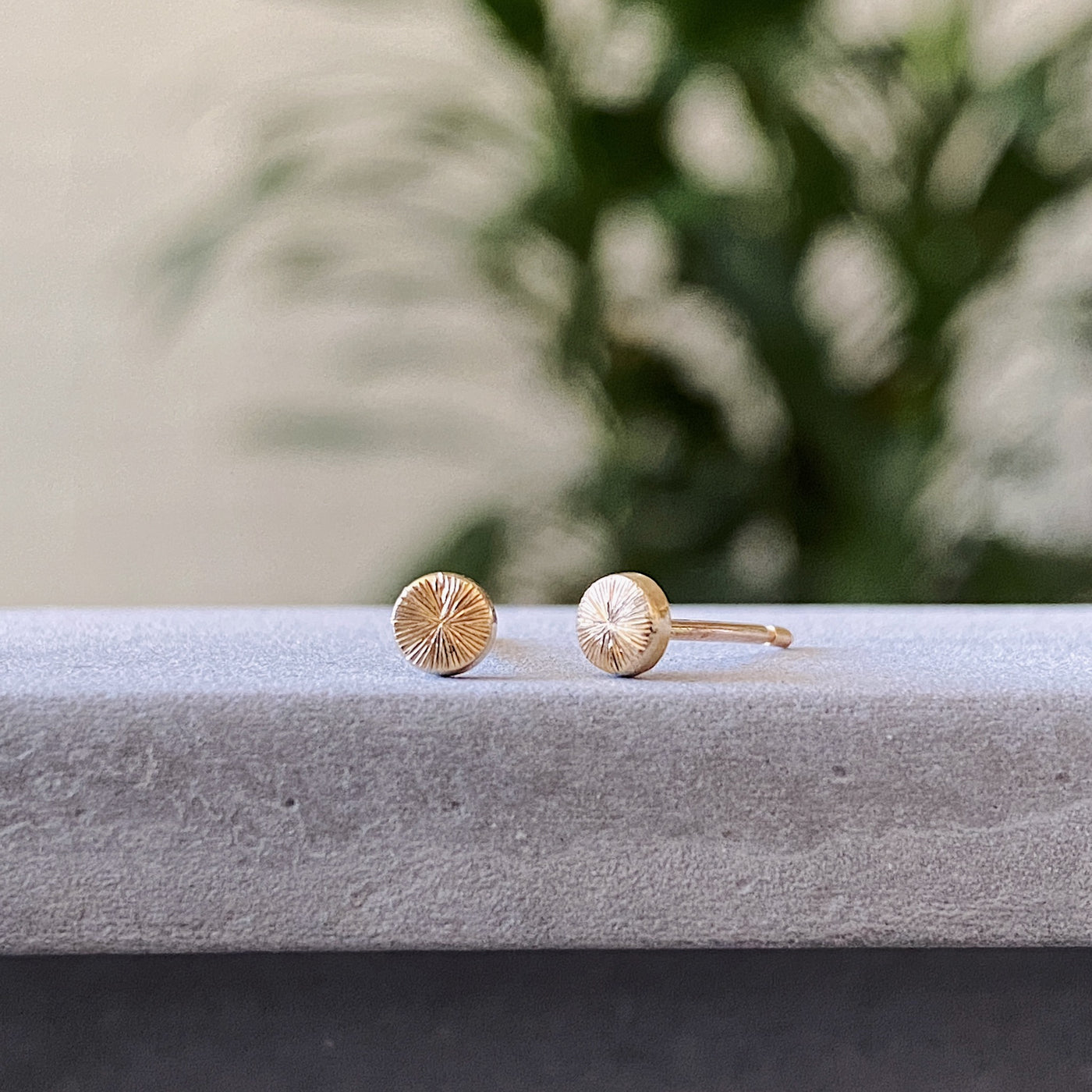 Tiny engraved gold stud earring by Corey Egan on concrete