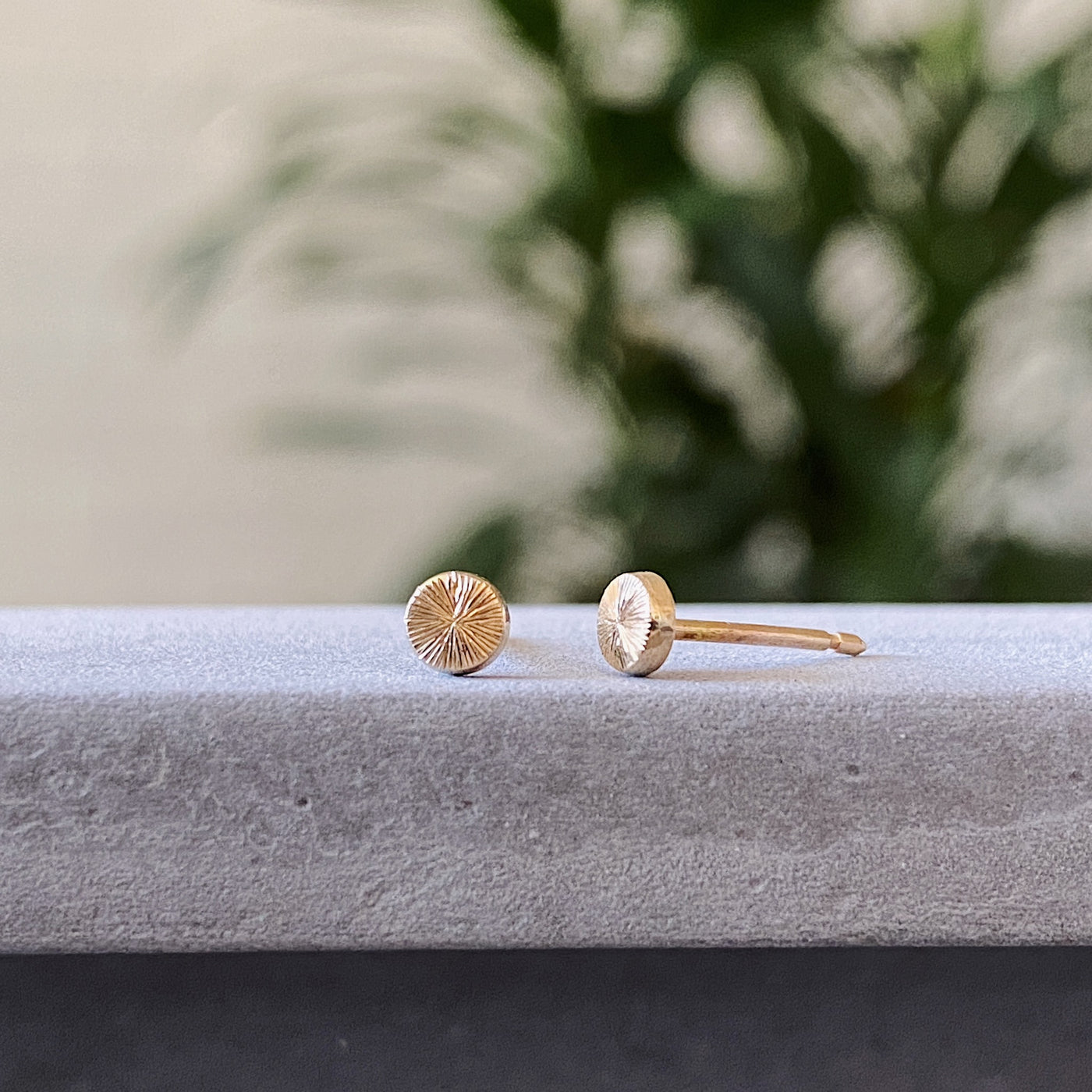 Tiny engraved gold stud earring by Corey Egan side view on concrete