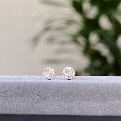 Tiny engraved silver stud earring by Corey Egan on concrete