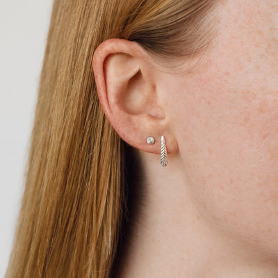 silver rise stud earrings with engraving on an ear with a herringbone stud earring