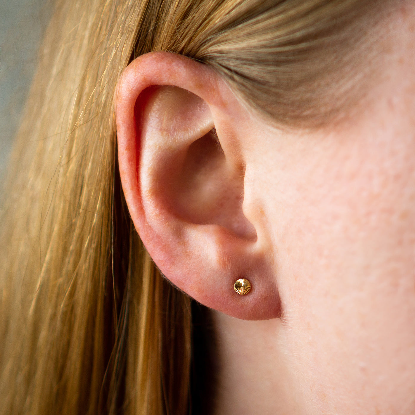 Tiny engraved gold stud earring by Corey Egan on an ear