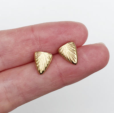 Triangular gold psark studs with carved sunburst design on two fingers by Corey Egan