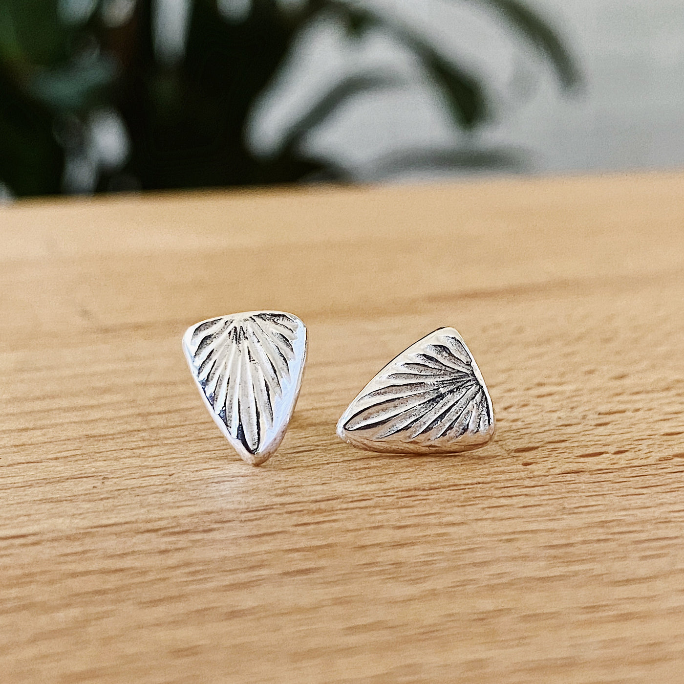 Sterling silver triangular stud earrings with a carved sunburst texture by Corey Egan on a tabletop view #2