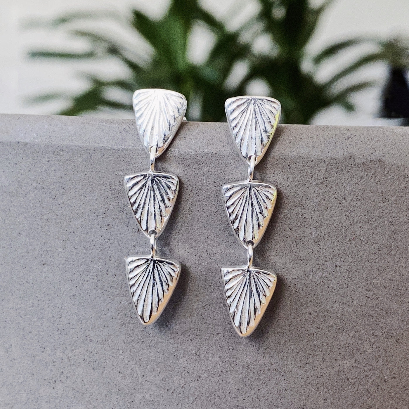 Sterling silver triple drop earrings of cared triangular sparks with post backs in natural light by Corey Egan