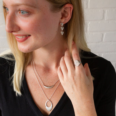 A model wearing the silver flicker earrings with two silver necklaces and the oval soleil signet ring with a diamond
