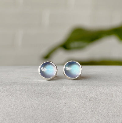 Moonstone stud earrings with silver bezel positioned forward in front of white wall