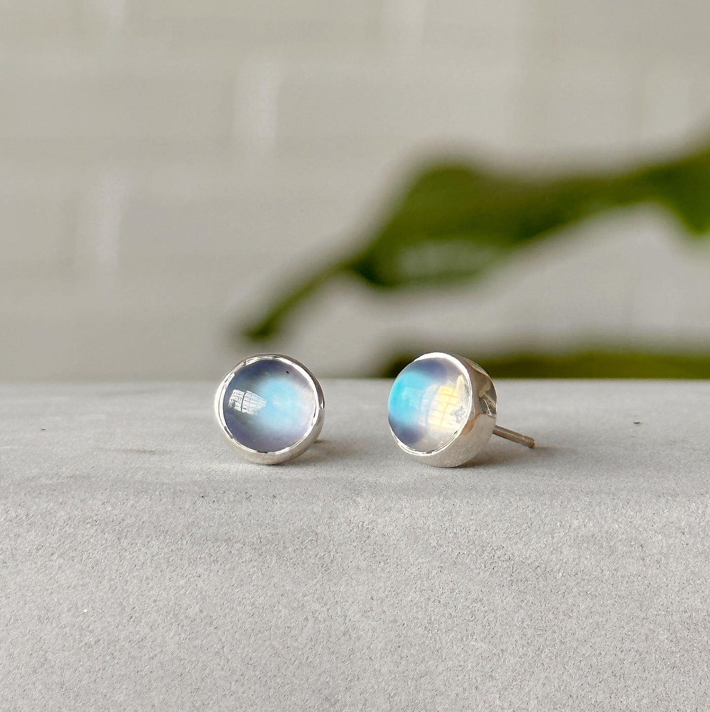 Moonstone stud earrings with silver bezel positioned sideways in front of white wall