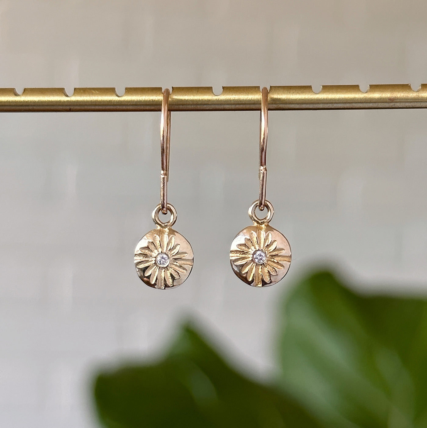 Small Lucia Gold Dangle Earrings hanging in front of a white wall, front angle