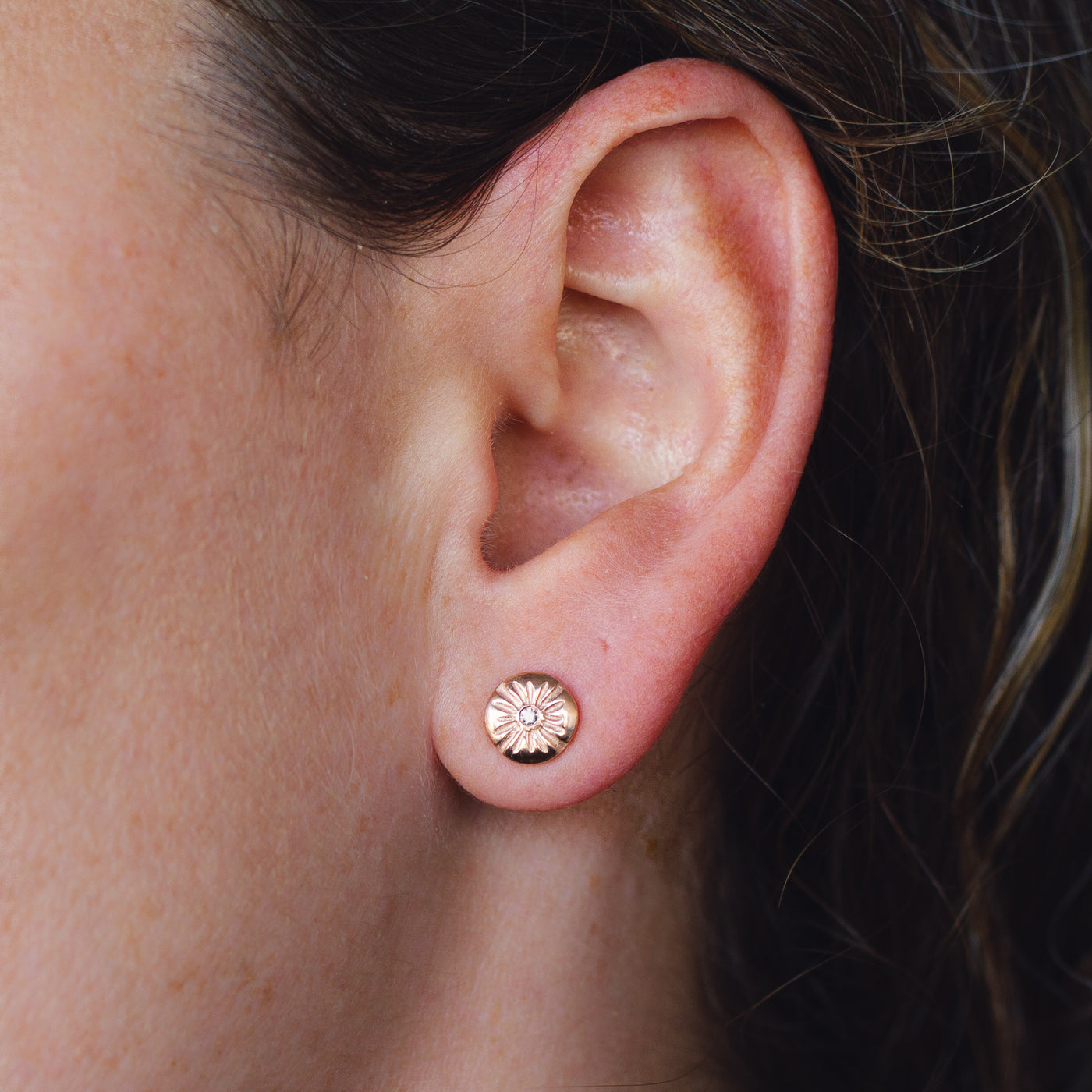 14k rose gold lucia stud earrings with white diamond centers on an ear