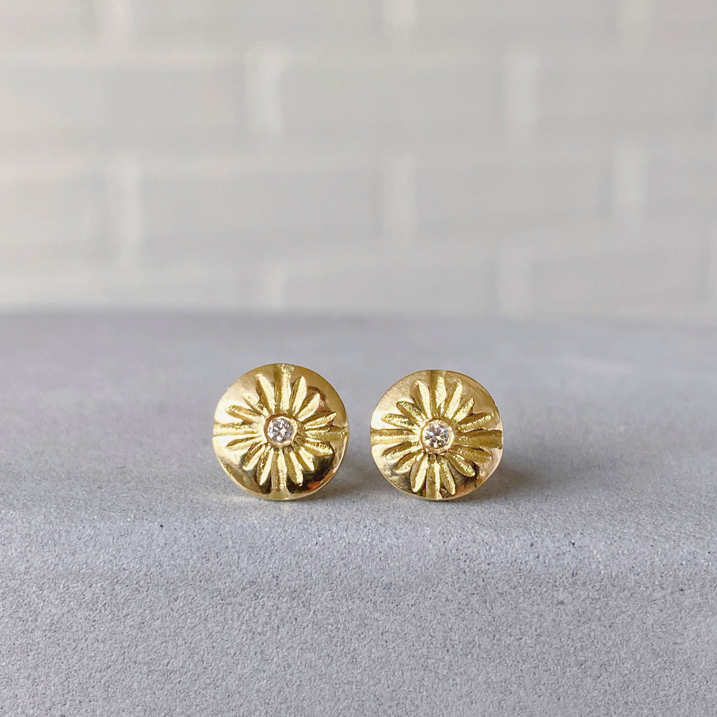 Small round carved sunburst stud earrings with diamond centers in gold in natural light
