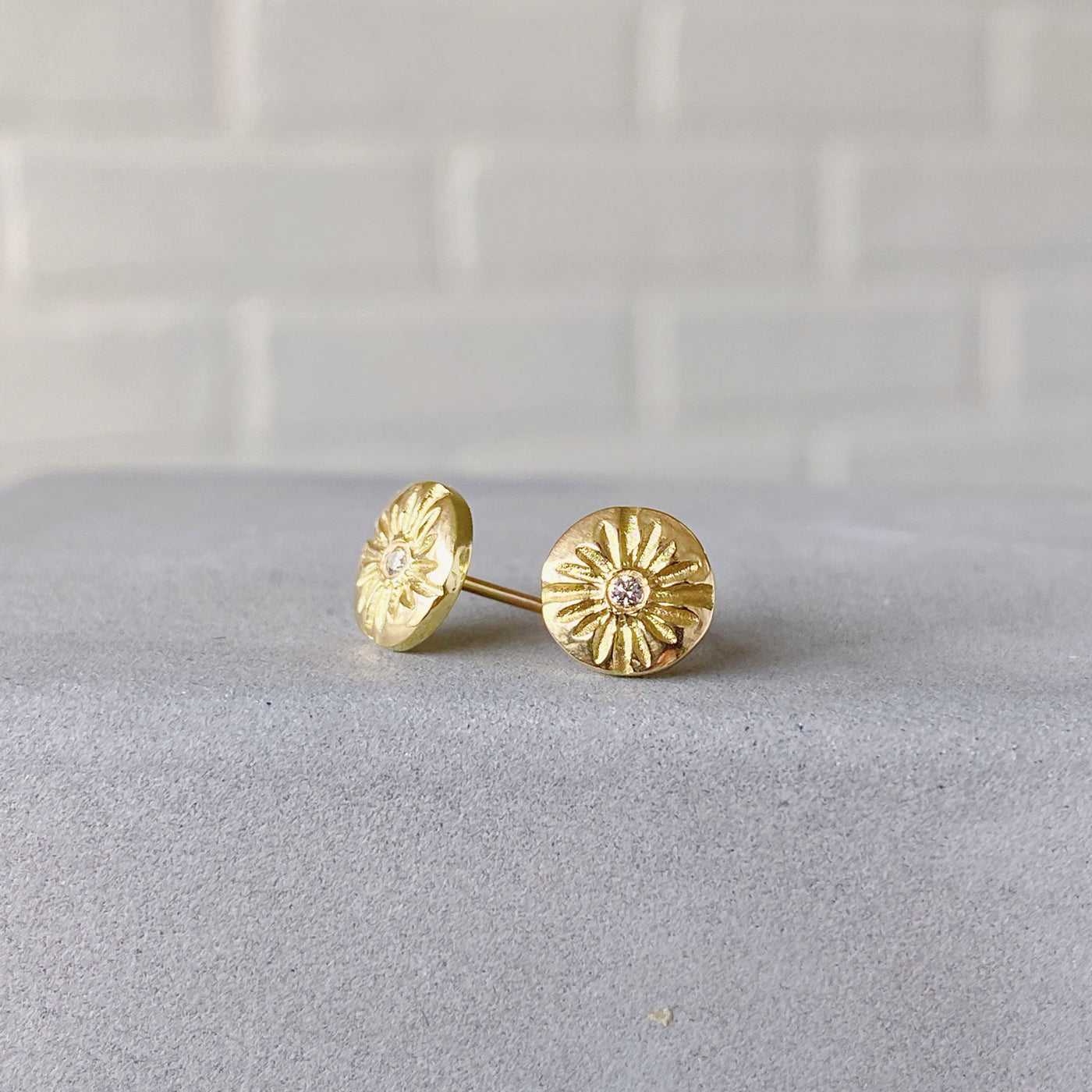 Small round carved sunburst stud earrings with diamond centers in gold in natural light side view