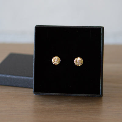 Small round carved sunburst stud earrings with diamond centers in gold in a gift box